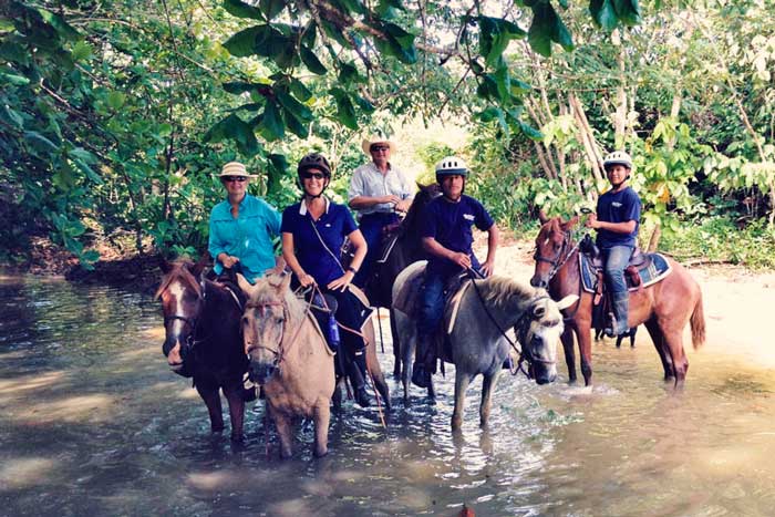 People riding horses through a river and rainforest of panama