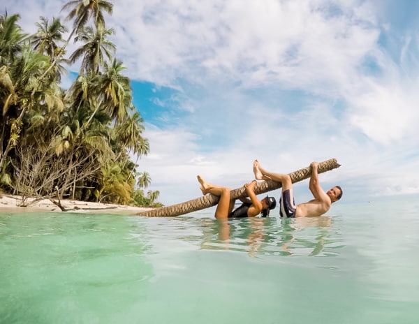 man and woman hanging on a palm tree over the water at Isla Zapatilla at Sol Bungalows Overwater Bungalows in Panama