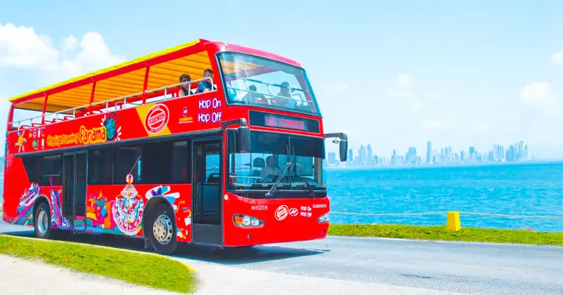 An image of the hop on hop off Bus in Panama city with the skyline of Panama city in the background and the ocean.