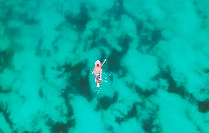 a man paddles on a surfboard on clear turquoise waters in bocas del toro panama 