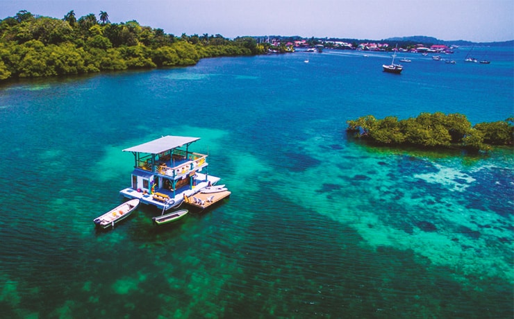 Drone view of the floating bar in bocas del toro with clear blue/green water and bocas town in the background.