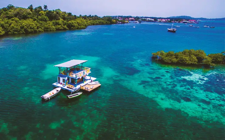 Drone view of the floating bar in bocas del toro with clear blue/green water and bocas town in the background.