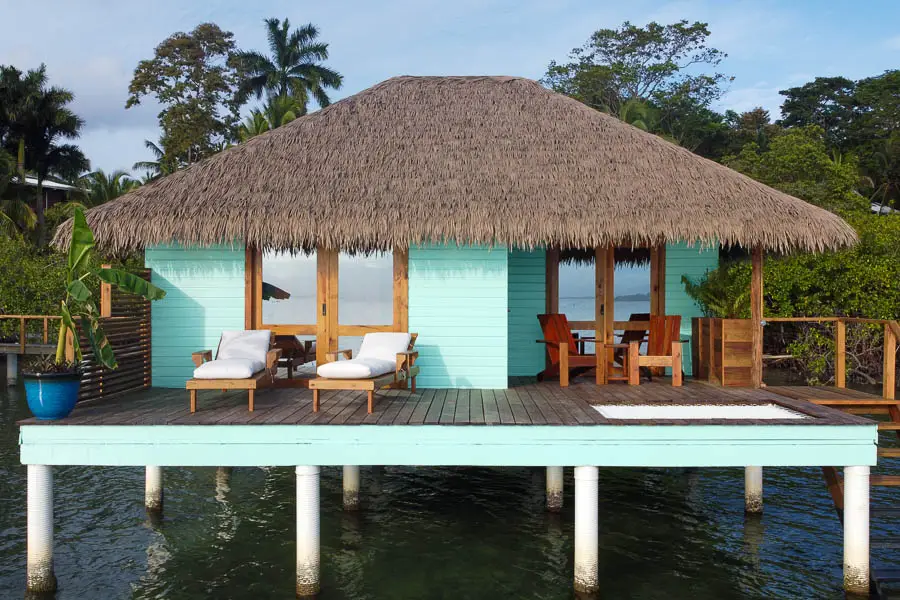 The frontal view of the overwater bungalow with turquoise paint and a thatch roof.