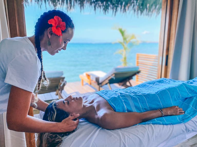 A massage at sol bungalows overwater bungalows with blue water int he background and a hibiscus leaf in the ear of the masseuse